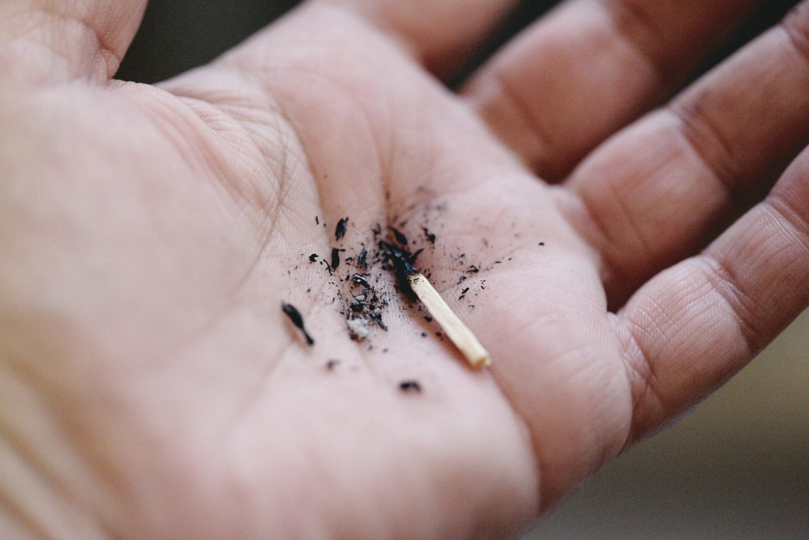 Detailed close-up of a palm holding burnt matchstick and charcoal residue, emphasizing texture.