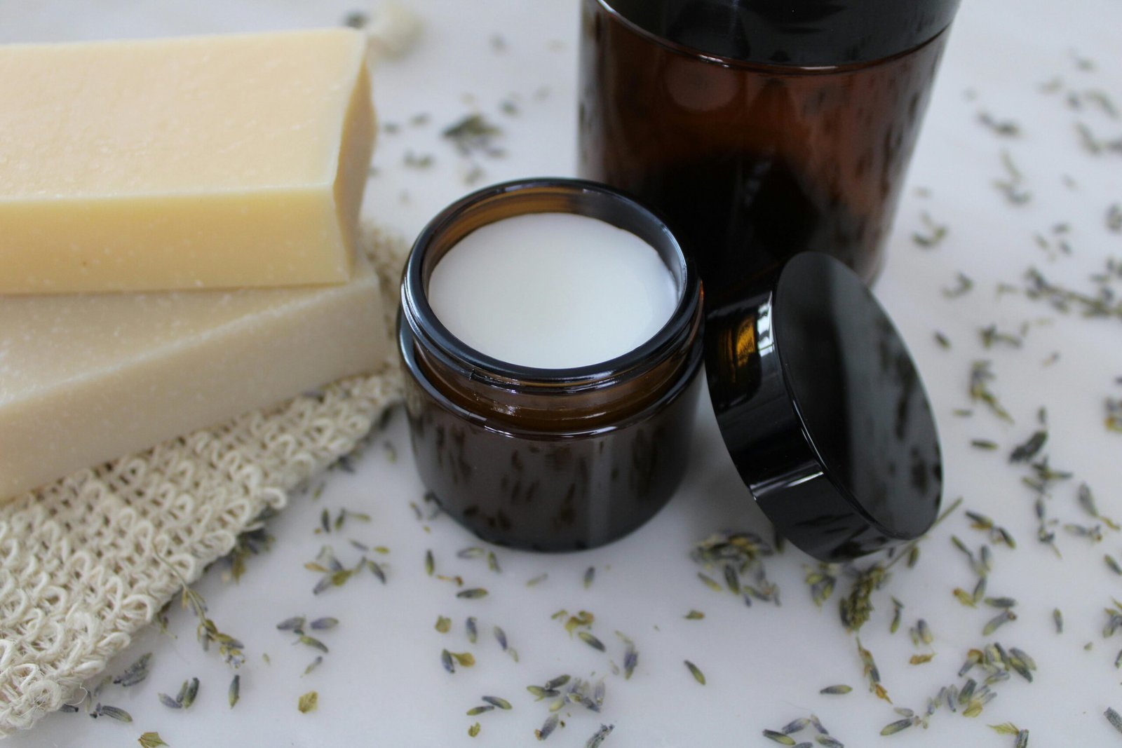 Organic bar soap and skin cream in amber jars with lavender sprigs on marble.